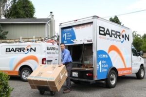 technician-with-boxed-HVAC-system-standing-in-front-of-Barron-truck